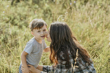 Mother kissing son on cheek in field - ANAF02081