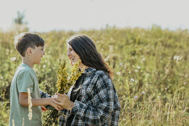 Lächelnde Mutter und Sohn halten einen Blumenstrauß auf einem Feld - ANAF02083