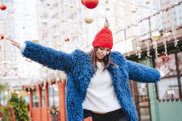 Smiling woman wearing blue coat dancing in city - NLAF00092