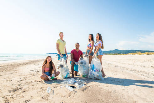 Group of eco volunteers holding bags with plastic after sorting waste - Friends cleaning the beach and collecting plastic to save marine life - DMDF04175