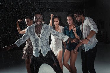 Eine Gruppe von Freunden tanzt im Regen - Multiethnische Menschen feiern eine Party - DMDF04211