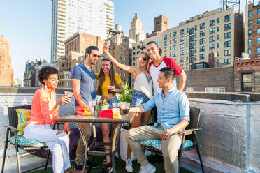 Junge, glückliche Menschen bei einem Grillabend auf einem Dach in New York - Eine Gruppe von Freunden feiert eine Party und hat Spaß - DMDF04263