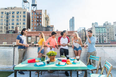 Junge, glückliche Menschen bei einem Grillabend auf einem Dach in New York - Eine Gruppe von Freunden feiert eine Party und hat Spaß - DMDF04306