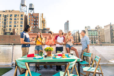 Junge, glückliche Menschen bei einem Grillabend auf einem Dach in New York - Eine Gruppe von Freunden feiert eine Party und hat Spaß - DMDF04316