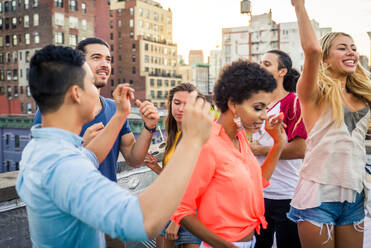 Young happy people having a barbecue dinner on a rooftop in New York - Group of friends having party and having fun - DMDF04326