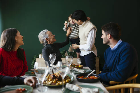 Grandmother tickling grandson by family having dinner at home - EBSF03771