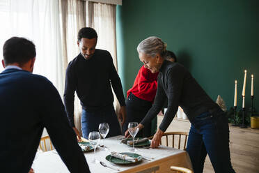 Familie deckt zu Hause den Tisch mit Tellern und Weingläsern - EBSF03773