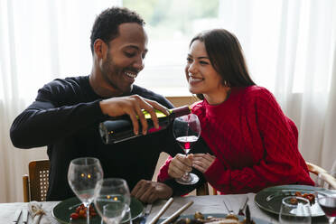 Lächelnder Mann schenkt einer Frau auf einer Dinnerparty Rotwein ein - EBSF03786