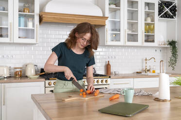 Young woman cutting carrot in kitchen - VPIF08644