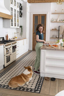 Frau schneidet Gemüse und sieht den Hund in der Küche an - VPIF08646