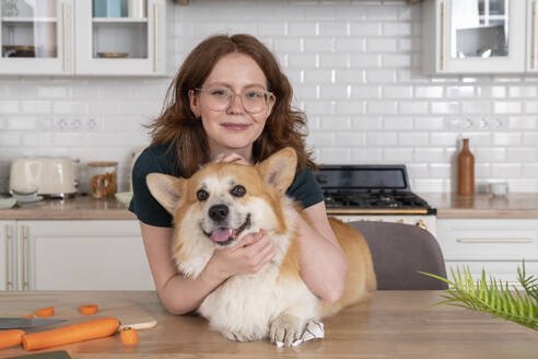 Lächelnde Frau mit Welsh Corgi Hund in der Küche - VPIF08650