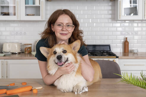 Smiling woman with Welsh Corgi dog in kitchen - VPIF08650
