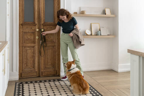 Frau mit Haustierleine betrachtet Welsh Corgi Hund, der zu Hause sitzt - VPIF08657