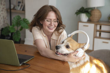 Happy woman wearing wireless headphones to dog at home - VPIF08677