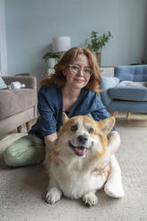Lächelnde Frau mit Welsh Corgi Hund zu Hause sitzend - VPIF08689