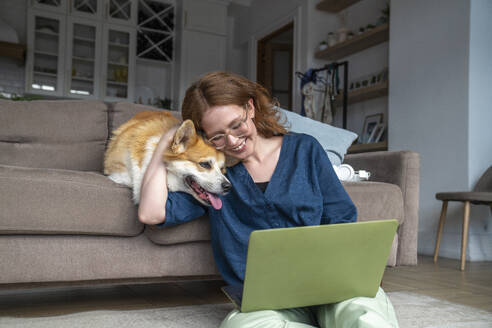 Lächelnde Frau mit Laptop, die ihren Hund zu Hause umarmt - VPIF08690