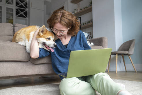 Lächelnder Freiberufler mit Laptop, der seinen Hund im Wohnzimmer umarmt - VPIF08691