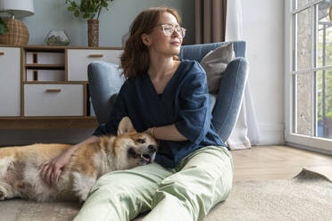 Welsh Corgi dog resting on woman's lap in living room - VPIF08698