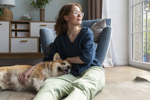 Welsh-Corgi-Hund auf dem Schoß einer Frau im Wohnzimmer liegend - VPIF08698