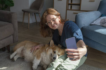 Woman taking selfie with pet dog on smart phone at home - VPIF08702