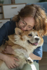 Woman hugging Welsh Corgi dog at home - VPIF08704