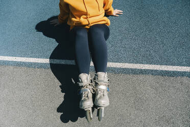 Woman wearing roller skates sitting at sports court - KANF00034