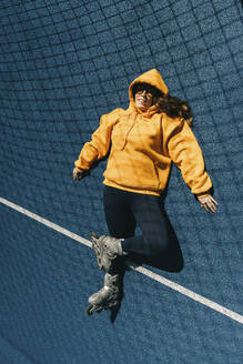 Frau mit Sweatshirt und Rollschuhen auf dem Sportplatz liegend - KANF00038