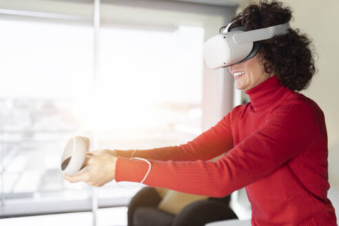 Lächelnde Frau mit Virtual-Reality-Headset beim Spielen zu Hause - JPTF01260