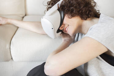 Lächelnde Frau mit Virtual-Reality-Headset, die sich zu Hause auf dem Sofa ausruht - JPTF01262