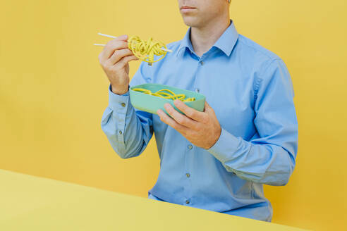 Man having wired noodles from lunch box in studio - YTF01125