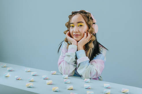 Junge Frau mit Kopfhörern sitzt am Tisch mit Marshmallows im Studio - YTF01126