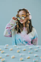 Woman with kaleidoscope and headphones sitting near marshmallows on table in studio - YTF01132