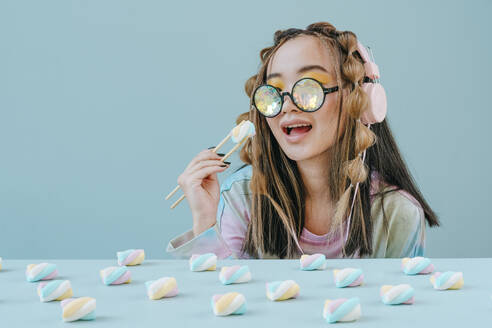 Frau mit Kaleidoskopbrille isst Marshmallows mit Stäbchen im Studio - YTF01134