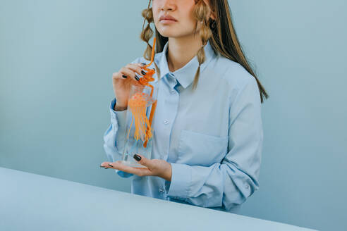 Frau hält Trinkglas mit Qualle und Strohhalm vor blauem Hintergrund - YTF01138