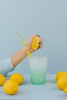 Hand einer Frau, die eine Zitrone im Cocktailglas auf dem Tisch auspresst - YTF01153