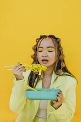 Junge Frau isst Nudeln wie Draht aus Bento-Box gegen gelben Hintergrund - YTF01165