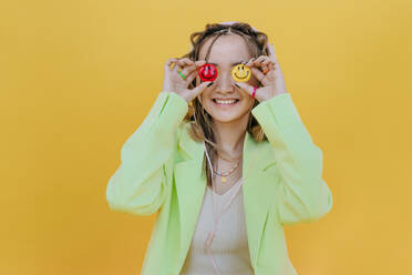 Smiling woman covering eyes with smileys against yellow background - YTF01171