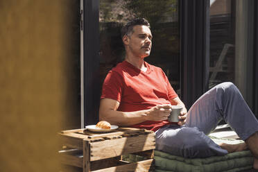 Man relaxing on balcony with mug in hand - UUF30076