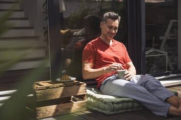 Man relaxing on balcony with mug in hand - UUF30079