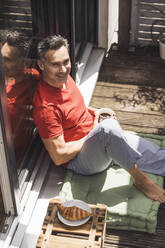 Mann entspannt auf Balkon mit Tasse in der Hand - UUF30085