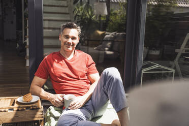 Man relaxing on balcony with mug in hand - UUF30086