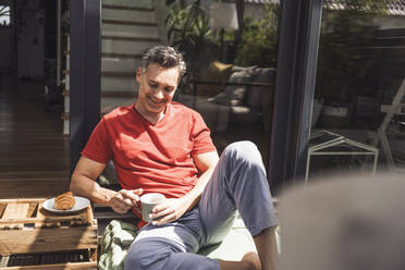 Man relaxing on balcony with mug in hand - UUF30087