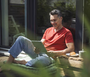 Mann entspannt auf Balkon mit digitalem Tablet in den Händen - UUF30088
