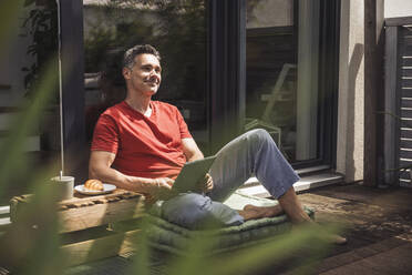 Mann entspannt auf Balkon mit digitalem Tablet in den Händen - UUF30089