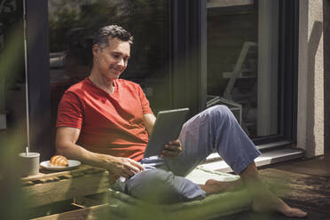 Man relaxing on balcony with digital tablet in hand - UUF30090