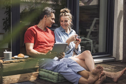 Ehepaar entspannt sich auf dem Balkon mit digitalem Tablet - UUF30093