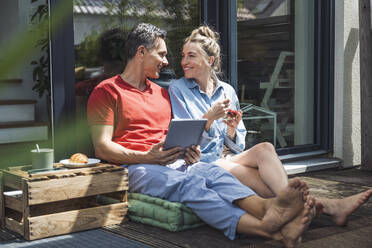 Ehepaar entspannt sich auf dem Balkon mit digitalem Tablet - UUF30094