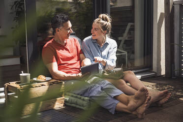 Ehepaar entspannt sich auf dem Balkon mit digitalem Tablet - UUF30096