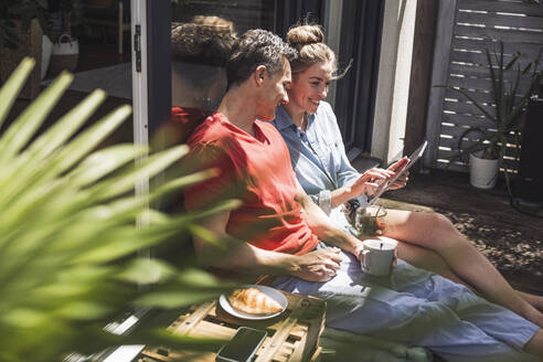 Ehepaar entspannt sich auf dem Balkon mit digitalem Tablet - UUF30102