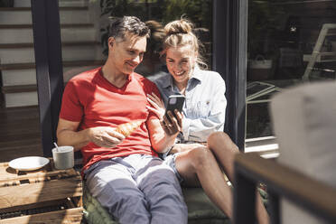 Ehepaar entspannt sich auf dem Balkon mit Smartphone - UUF30105